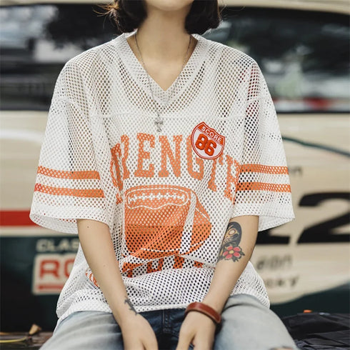 Person wearing a white mesh jersey with orange text and graphics, sitting in front of a blurred background.
